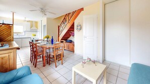 A spacious living area with a dining table, chairs, a sofa, and a small table with decorative items. A staircase leads to an upper level.