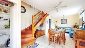 A spacious living area with a wooden staircase, a dining table set for four, and a blue sofa.