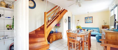 Un vaste espace de vie agrémenté d’un escalier en bois, d’une table à manger pour quatre personnes et d’un canapé bleu.