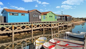 A wooden pier with colorful wooden buildings, boats docked at the end, and calm water reflecting the structures.