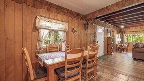 A wooden dining area with a table and chairs, a window with curtains, and a door leading to another room.