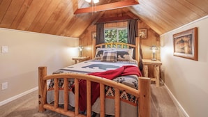 A cozy bedroom with a wooden ceiling, a bed with a patterned bedspread, two bedside tables with lamps, and a window with curtains.