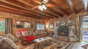 A cozy living room with a stone fireplace, leather sofas, and a wooden ceiling fan.