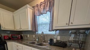 A kitchen with white cabinets, a granite countertop, a stainless steel sink, a microwave, and a stove. - Rock Scene Arcade, Retro Rock & Arcade games. (Houston)