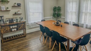 Un comedor con una mesa y sillas de madera, una barra de café con estanterías y plantas, y un letrero que dice "Coffee BAR".