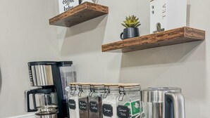 Una estación de café con cafetera, molinillo y hervidor, junto con recipientes etiquetados para café, azúcar y té.