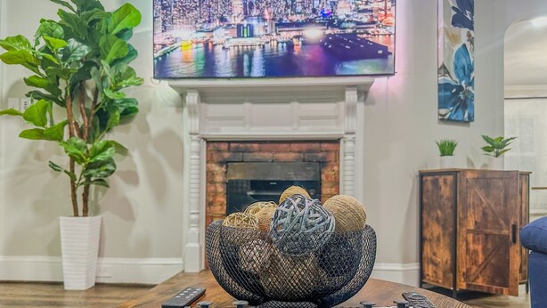 Un salón con chimenea, una planta grande en maceta y dos mandos de consola sobre una mesa de centro de madera.