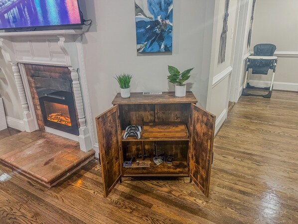 Un salón con chimenea, televisor, un mueble de madera con una planta y un cambiador para bebés.