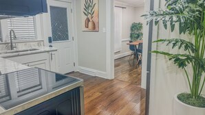 Una cocina moderna con horno empotrado, un comedor con mesa y sillas de madera, y una planta grande en maceta.
