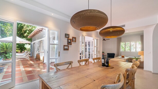 A spacious dining area with a large wooden table and chairs, surrounded by large windows and doors leading to an outdoor patio area. - Beautiful home in Canyamel with private swimming pool, can be inside or outside (Canyamel)