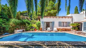 A swimming pool with a patio area, surrounded by lush greenery and a white building with blue shutters. - Beautiful home in Canyamel with private swimming pool, can be inside or outside (Canyamel)