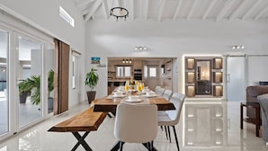 A spacious dining area with a long wooden table, white chairs, and a modern chandelier.