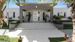 A modern two-story house with a flat roof, white exterior, and a front entrance with steps.