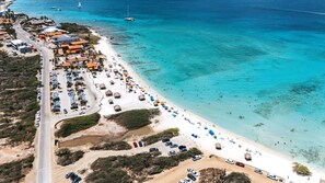 Luftaufnahme einer Küstenregion mit Strand, geparkten Autos und einer Straße.
