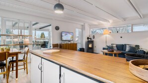 Et moderne køkken med træbordplade, hvide skabe og et stort vindue med udsigt til et sneklædt landskab.