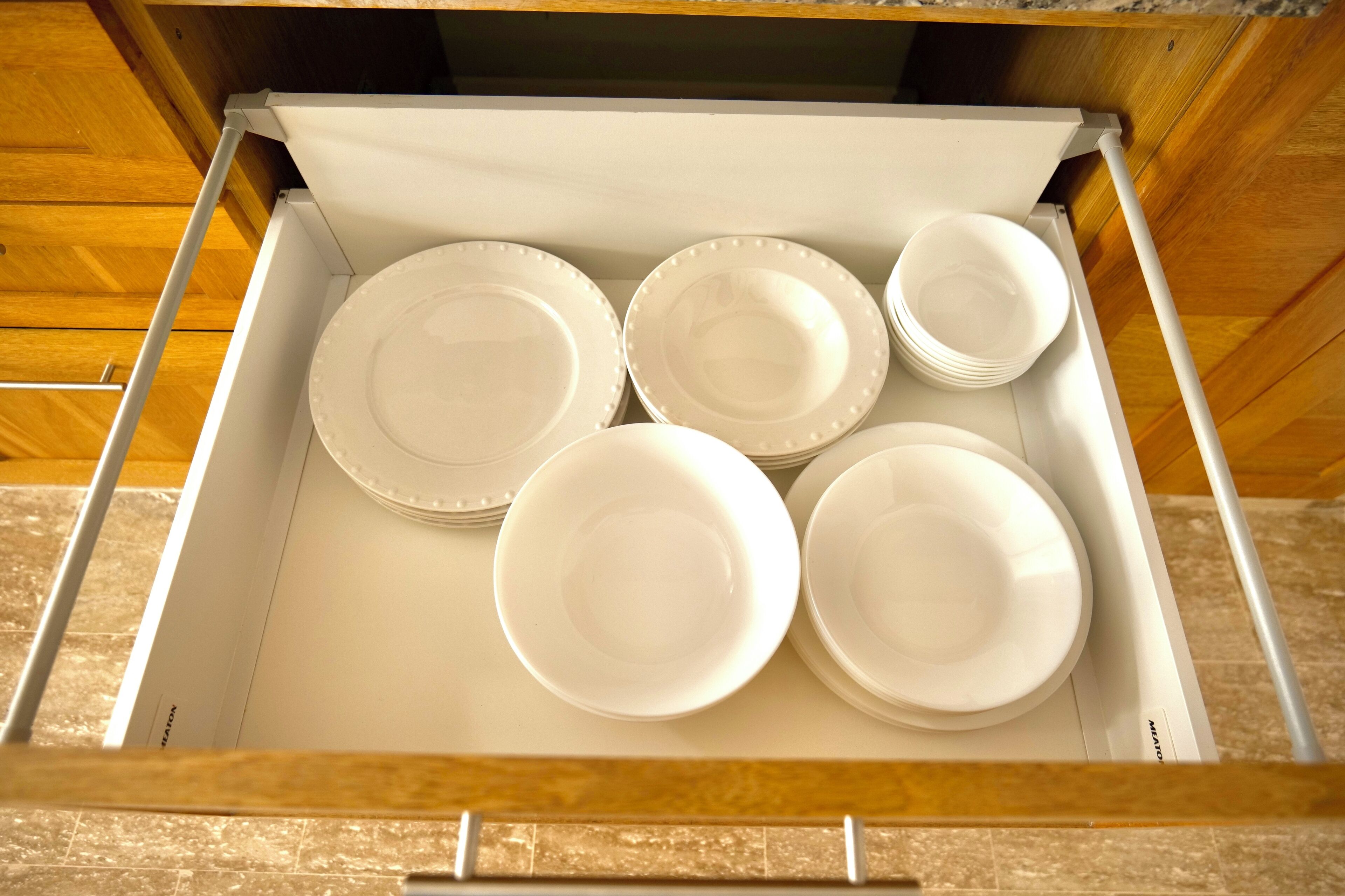 A drawer with white plates and bowls.