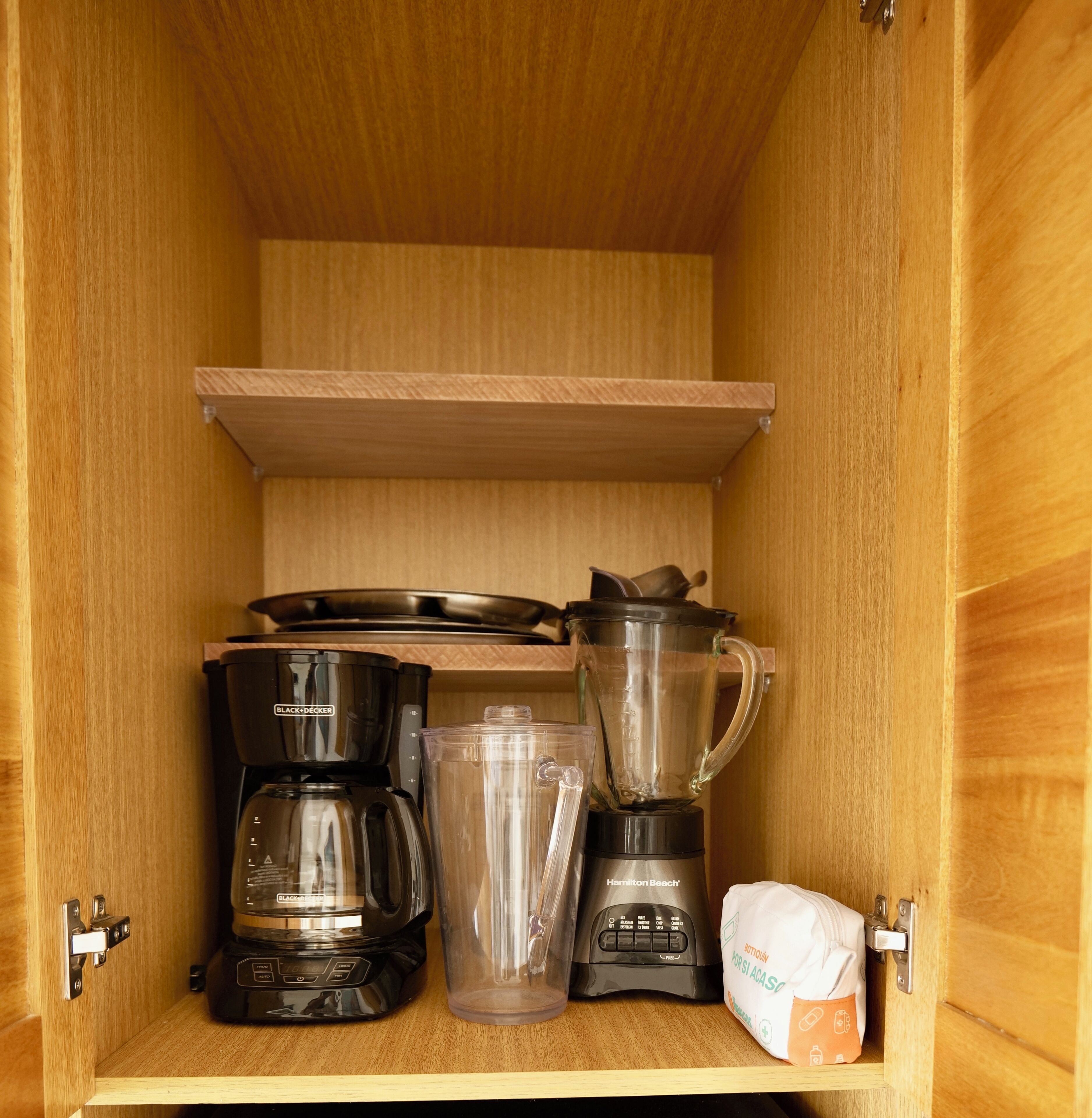 Ett köksskåp med en kaffebryggare, en mixer och en förpackning blöjor.