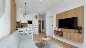 A modern living room with a large TV, wooden paneling, a dining area, and a kitchen in the background. - Amazing apartment in Ustronie Morskie (Ustronie Morskie)