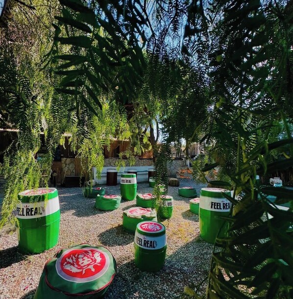 Un espace aménagé en jardin, avec des barils verts portant l'inscription « FEEL REAL » et un élément décoratif aquatique.