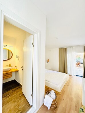 Une chambre d’hôtel avec un plancher en bois, un lit, une salle de bain avec un lavabo et un miroir, et une vue sur l’extérieur.