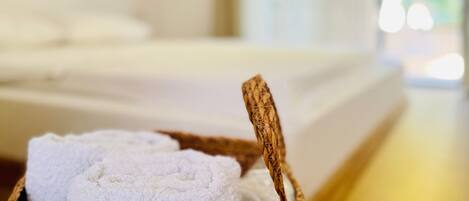 Una cama con ropa blanca, un cabecero de madera, una toalla blanca y una cesta tejida.