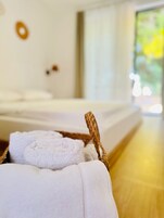 Una cama con ropa blanca, un cabecero de madera, una toalla blanca y una cesta tejida.