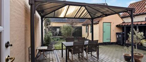 A covered patio with a table and chairs, a door, and a small garden area.