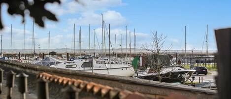 A marina with multiple boats docked, a clear sky, and a distant view of land.