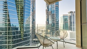 A balcony with two wicker chairs and a glass table, overlooking modern high-rise buildings. - Vibrant 2BR, Miami Vibes at Business Bay (Dubai)