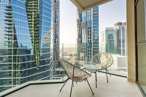 A balcony with two wicker chairs and a glass table, overlooking modern high-rise buildings. - Vibrant 2BR, Miami Vibes at Business Bay (Dubai)