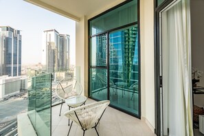 A balcony with two wicker chairs, a glass table, and a view of tall buildings. - Vibrant 2BR, Miami Vibes at Business Bay (Dubai)