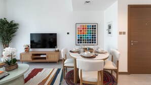 A modern living room with a flat-screen TV, a dining table set for four, and a colorful abstract painting on the wall. - Vibrant 2BR, Miami Vibes at Business Bay (Dubai)