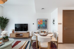 A modern living room with a flat-screen TV, a dining table set for four, and a colorful abstract painting on the wall. - Vibrant 2BR, Miami Vibes at Business Bay (Dubai)