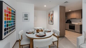 A modern dining area with a round table set for four, white chairs, and a kitchen in the background. - Vibrant 2BR, Miami Vibes at Business Bay (Dubai)