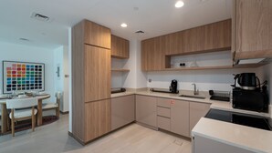 A modern kitchen with wooden cabinets, a dining area with a table and chairs, and a coffee machine. - Vibrant 2BR, Miami Vibes at Business Bay (Dubai)