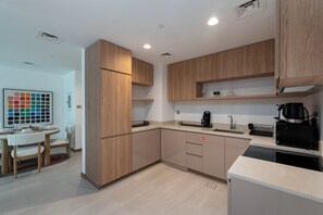 A modern kitchen with wooden cabinets, a dining area with a table and chairs, and a coffee machine. - Vibrant 2BR, Miami Vibes at Business Bay (Dubai)