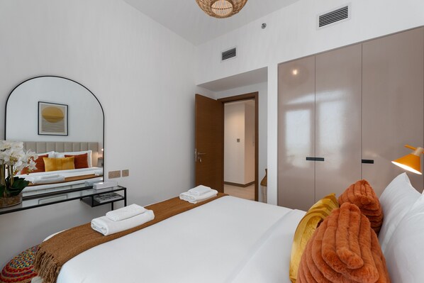 A modern hotel room with a large bed, a bedside table with a lamp, a mirror, and a view of the hallway.