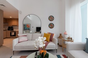 A modern living room with a sofa, coffee table, and a dining area with a table and chairs. - Vibrant 2BR, Miami Vibes at Business Bay (Dubai)