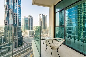 A high-rise building with a glass balcony, white wicker chairs, and a cityscape view.
