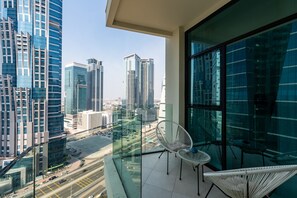 A balcony with a glass railing, white chairs, and a view of tall buildings.