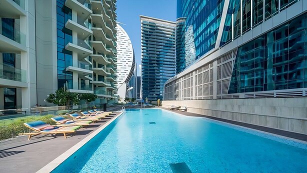 A modern hotel with a swimming pool, high-rise buildings, and a clear sky. - Vibrant 2BR, Miami Vibes at Business Bay (Dubai)