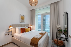 Ein modernes Hotelzimmer mit einem großen Bett, einem Nachttisch mit Lampe, einem Spiegel und Blick auf die Stadt durch das Fenster.