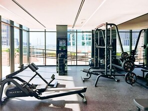 A gym with cardio equipment, weightlifting stations, and large windows offering city views.