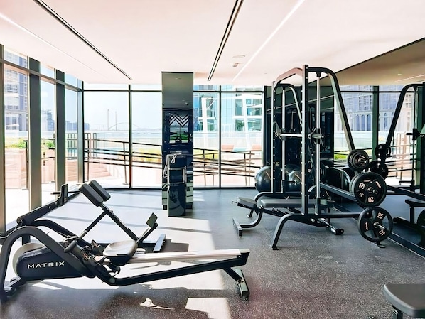 Ein Fitnessstudio mit Cardiogeräten, Krafttrainingsgeräten und großen Fenstern mit Blick auf die Stadt.