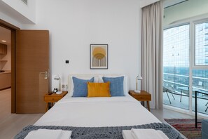 A modern hotel room with a large bed, two bedside tables, a window with a city view, and a wooden door. - Vibrant 2BR, Miami Vibes at Business Bay (Dubai)