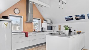 Una cocina moderna con armarios blancos, una isla central, una campana extractora de acero inoxidable y un reloj en la pared.