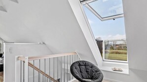 Un dormitorio estilo loft moderno con tragaluces, una escalera de madera y una silla negra junto a la ventana.