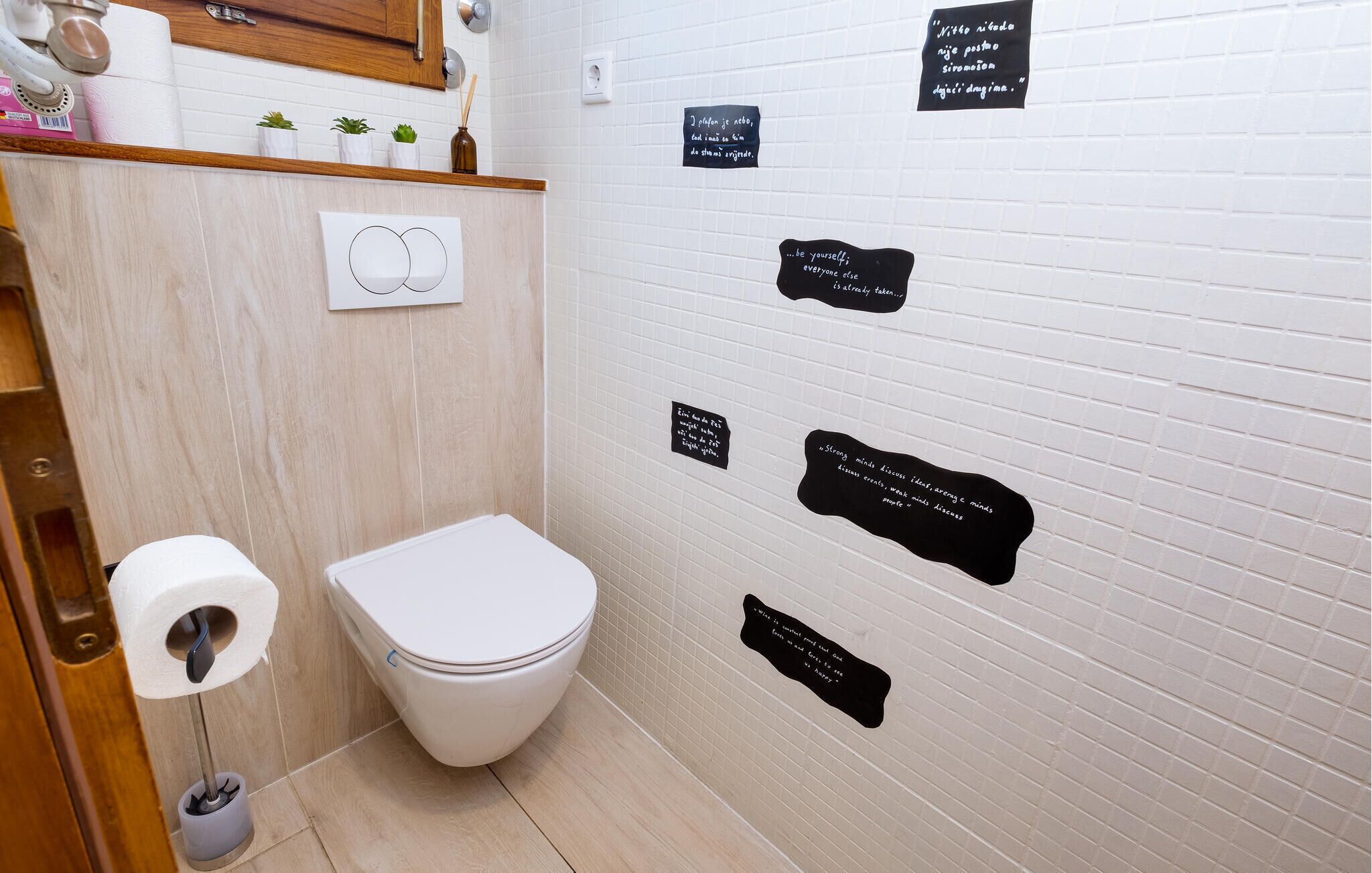 Une salle de bain équipée de toilettes, d’un distributeur d’essuie-tout et d’un sèche-mains. Plusieurs affiches motivantes sont accrochées au mur.