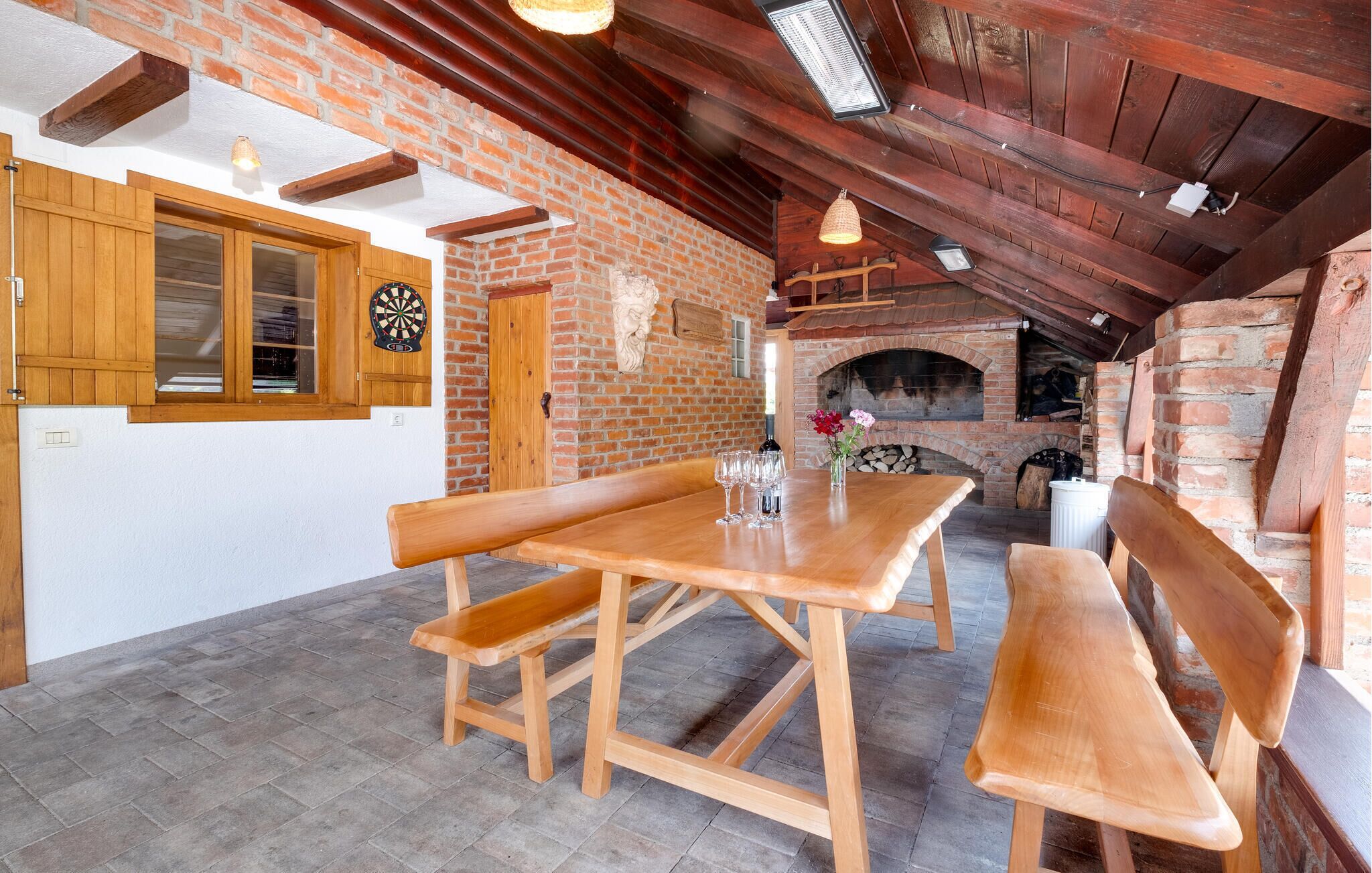 Een rustieke keuken met een bakstenen muur, houten balken, een houten tafel met banken en een bakstenen open haard.