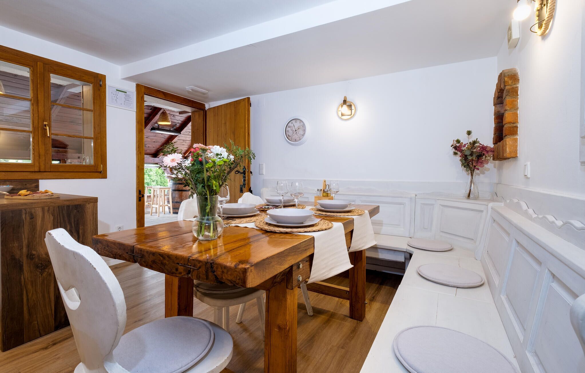 Un coin repas avec une table en bois dressée pour quatre personnes, des chaises blanches et un vase de fleurs.